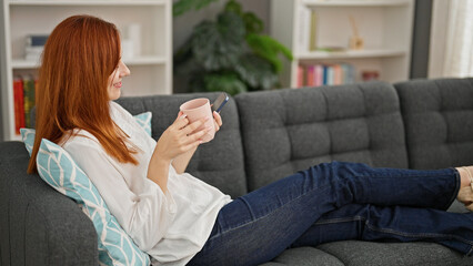 Young redhead woman using smartphone drinking coffee at home
