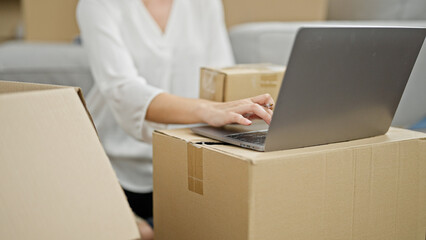 Young redhead woman using laptop holding package at new home