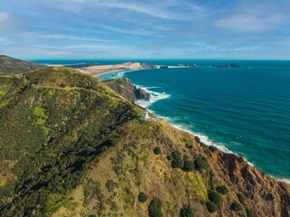 Aerial view of sea waves crashing against green coastal mountains on a sunny day