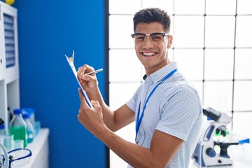Young hispanic man scientist writing on document at laboratory