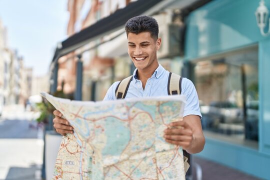 Young hispanic man student smiling confident holding city map at street
