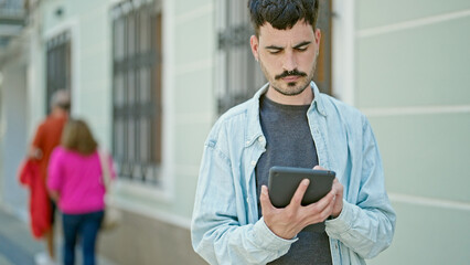 Young hispanic man using touchpad with relaxed expression at street