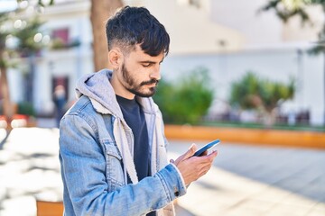 Young hispanic man using smartphone at park