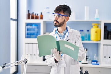 Young hispanic man scientist writing on notebook working at laboratory