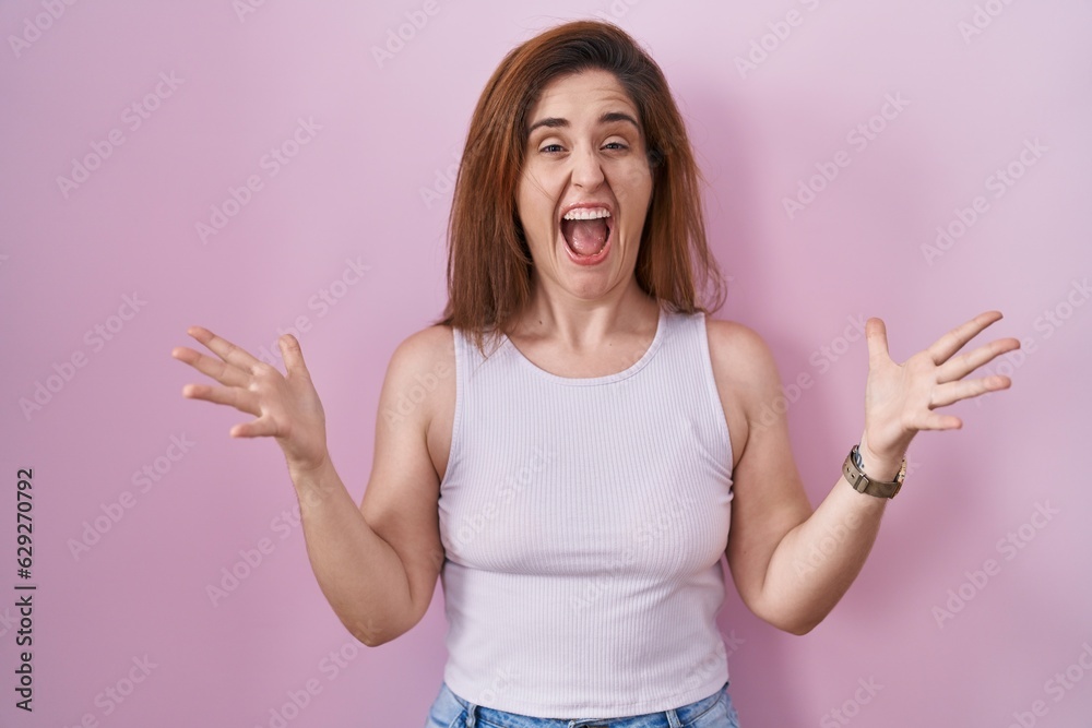 Sticker Brunette woman standing over pink background celebrating crazy and amazed for success with arms raised and open eyes screaming excited. winner concept