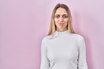 Fototapeta premium Young blonde woman wearing white sweater over pink background depressed and worry for distress, crying angry and afraid. sad expression.