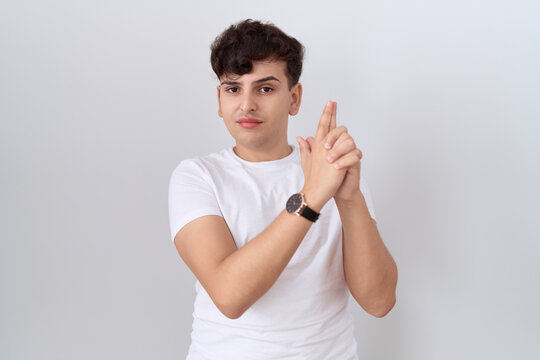 Young non binary man wearing casual white t shirt holding symbolic gun with hand gesture, playing killing shooting weapons, angry face