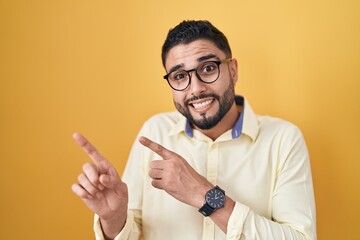 Hispanic young man wearing business clothes and glasses pointing aside worried and nervous with...