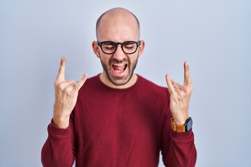 Naklejka premium Young bald man with beard standing over white background wearing glasses shouting with crazy expression doing rock symbol with hands up. music star. heavy music concept.