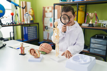 Adorable hispanic girl scientist student using magnifying glass at laboratory classroom