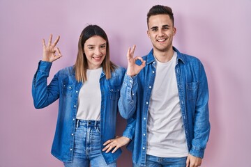 Fototapeta premium Young hispanic couple standing over pink background smiling positive doing ok sign with hand and fingers. successful expression.