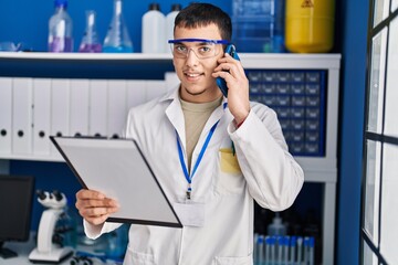 Young man scientist talking on the smartphone reading document at laboratory