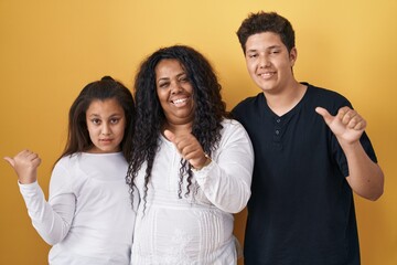 Family of mother, daughter and son standing over yellow background pointing to the back behind with...