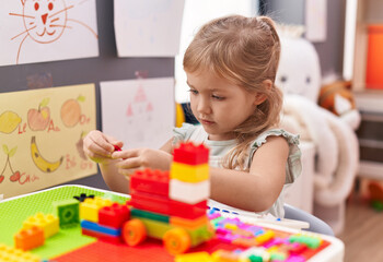 Adorable blonde girl playing with construction blocks sitting on table at kindergarten