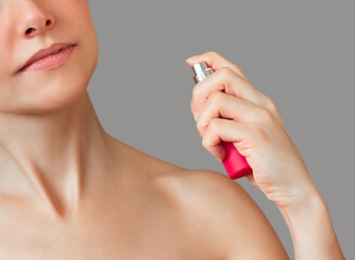 A young beautiful Caucasian woman with open shoulders spraying perfume from a pink bottle on her neck
