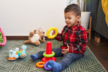 Obraz premium Adorable hispanic boy playing with hoops game sitting on floor at home