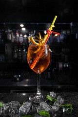 Glass of craft cocktail with ice cubes, lemon slices, and garnish against the backdrop of a bar