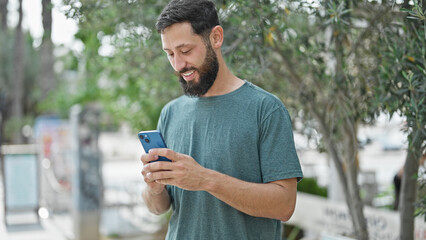 Fototapeta premium Young hispanic man using smartphone smiling at park
