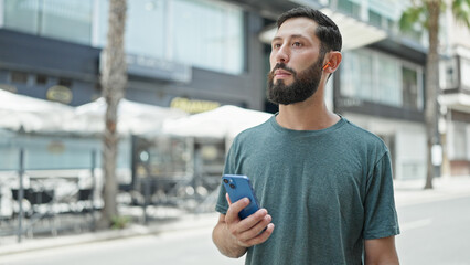 Young hispanic man using smartphone and earphones at street