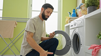 Obraz premium Young hispanic man washing clothes at laundry room