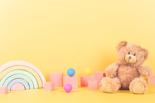 Educational kids toys collection. Teddy bear, wooden rainbow pink cubes and colorful balls on yellow background. Front view