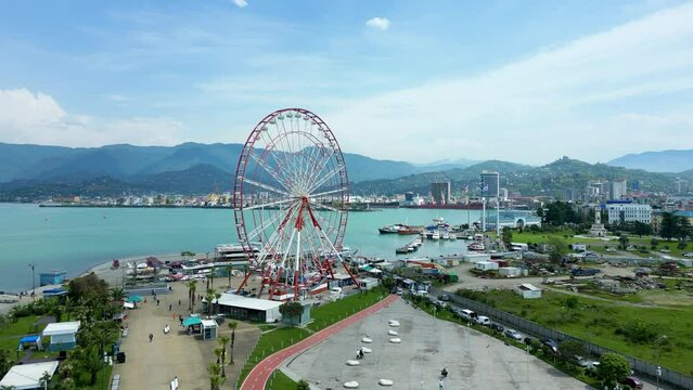 Drone view of a Ferris Wheel located on a harbor with a background of buildings and mountains