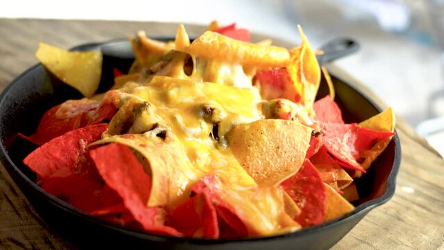 Close-up view of cheesy nachos in a pan on a wooden board