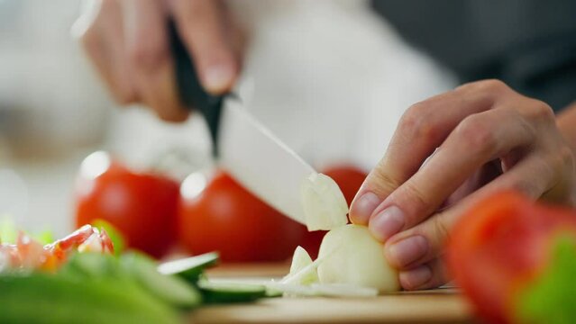 Woman is slicing onion on a wooden cutting board. Chopped tomatoes, cucumbers, onions, lettuce for making village salad. Hands are dicing onions, other ingredients on board. Greek salad or horiatiki