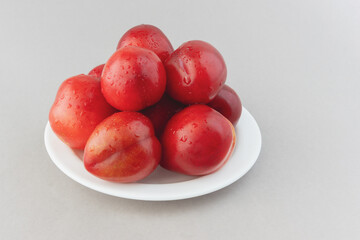 Fresh orange plums in a plate on a gray background