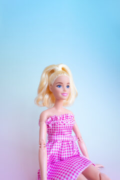 座って前を見ている笑顔のバービー人形 - 水色からピンクのグラデーションの背景