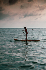 Fototapeta na wymiar Young woman in silhouette having fun on her SUP in the calm sea of sunset