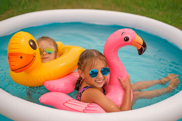 Beautiful girls relax at home in a mini plastic pool, splashing together with inflatable circles in the shape of birds