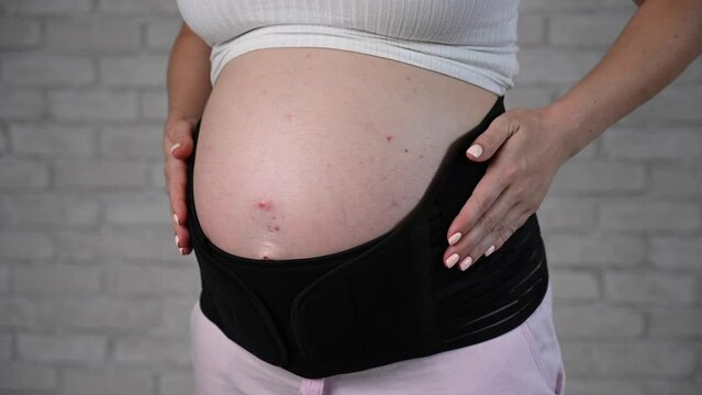 A pregnant woman puts on a black two-piece bandage. Cropped tummy. 