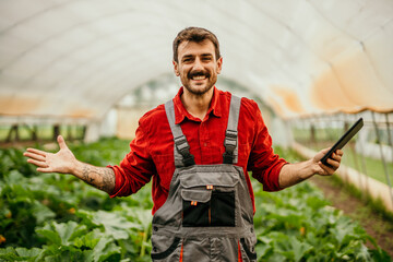 Portrait of a smiling farmer holding a digital tablet while working in a greenhouse.