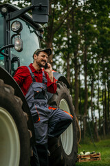 Smiling farmer talking on a mobile phone in front of a tractor in the field. Smart farming concept