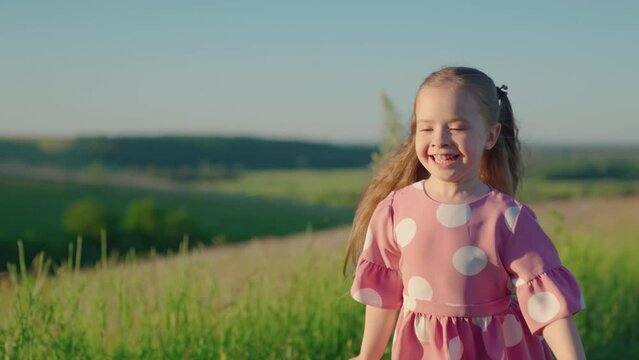 Little happy girl runs on grass, smiles, in slow motion. Childhood dream concept. Kid runs across meadow. Happy running child in field. Happy family. Cheerful little girl playing in park in summer.
