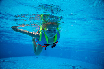Obraz na płótnie Canvas Portrait of little girl swimming underwater in goggles and vest in pool. Summer vacation