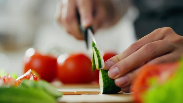 Preparing the concept of healthy food. Close-up of female hands slicing cucumber for a salad. Cooking an eco-friendly organic lunch. Woman is cutting cucumber on a cutting board in her home kitchen