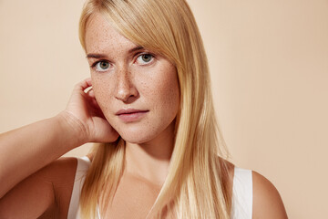 Young beautiful blond woman with freckles looking at the camera and adjusting her hair