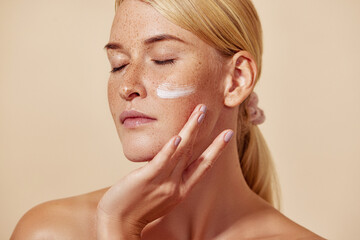 Beautiful young female with closed eyes applying white cream on her face - Powered by Adobe