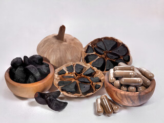 one whole and one cut across black fermented garlic bulb next to wedges and capsules isolated on white background