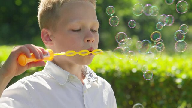 Happy caucasian boy having fun with soap bubbles at sunny day. Child play. Happy time. Boy having fun outdoors. 4K, UHD
