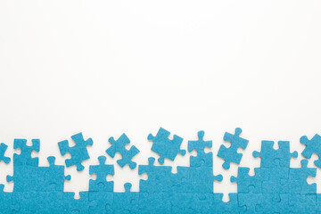 Unfinished blue puzzle pieces on white table background. Closeup. Empty place for text. Top down view.