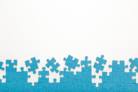 Unfinished blue puzzle pieces on white table background. Closeup. Empty place for text. Top down view.