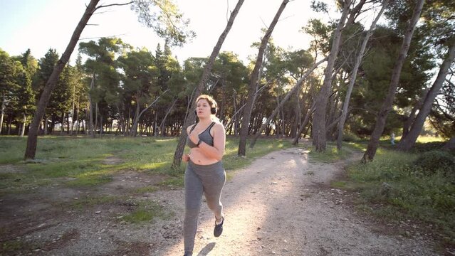 Bodypositive plus size female athlete jogging in the sunny park. Concept of weight loss and active lifestyle