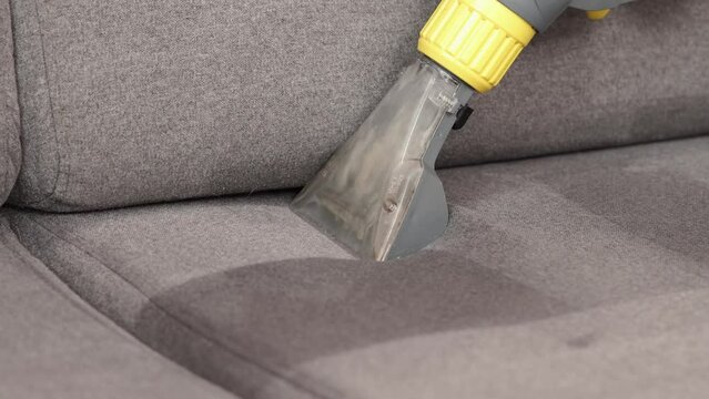 Dry cleaner's man employee removing dirt from furniture in flat, closeup, vacuum clean sofa with professional equipment. cleaning sofa with washing suction cleaner closeup.