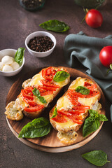 Baked brioche sandwiches with tomatoes, mozzarella and basil on a cutting board vertical view