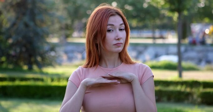 In the park, a young girl looks at the camera and makes gestures and facial expressions indicating disapproval, appearing definite and saying "no"