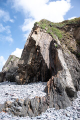 Coastal outcrop, with vertical rock strata, stands behind a beach full of pebbles and boulders