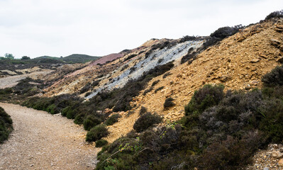 Multi colored spoil heaps stand next to a roadway in a quarry.